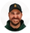 Circular headshot of a smiling bearded man in a dark cap and dark green shirt.