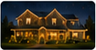 Nighttime residential exterior photo of a warmly illuminated home with holiday lights.