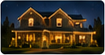 Nighttime residential exterior photo with a warmly lit house and golden holiday lighting.