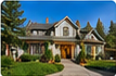 Daytime front exterior photograph of a gray gabled house with a landscaped lawn and driveway.